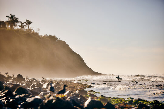 Distant view of person standing with surfboard in sea against sky
