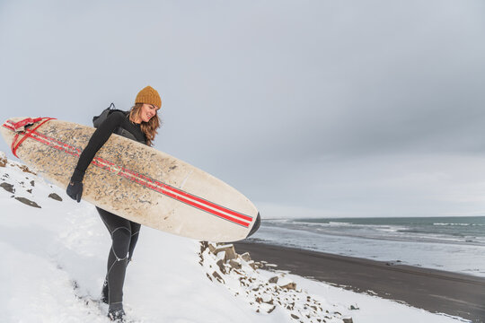 Woman walking on beach with surf board winter iceland