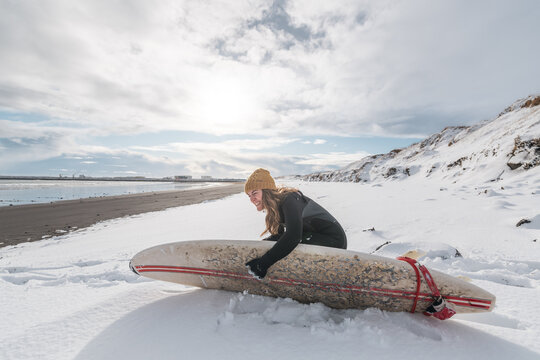 Woman standing on beach with surf board winter iceland