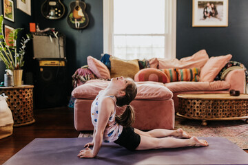 Young girl does upward facing dog on yoga mat in living room