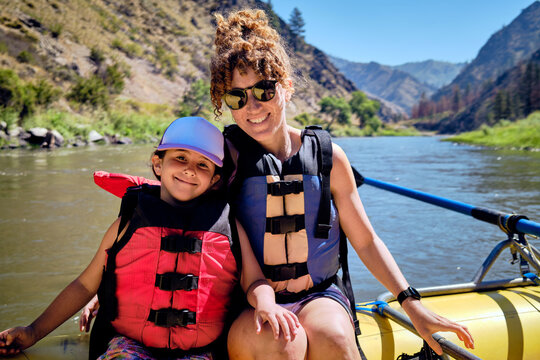 Smiling mother and daughter sitting in inflatable raft on salmon river