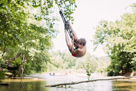 Boy hanging on rope swing from tree during summer