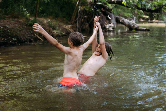 Preteen boys playing on rope swing in water during summer