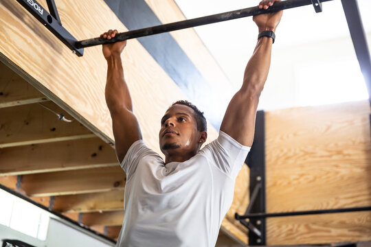 Fit Man in White T-Shirt Hanging from Chin-up Bar in Gym - Powered by Adobe