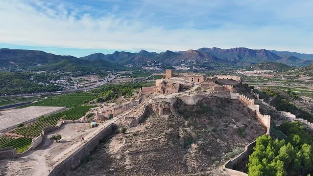 cinematic flight with a dro at the highest part of the Sagunto castle watching people visiting it and with a beautiful background of mountains and a blue sky and white clouds filmed in 70mm in Spain