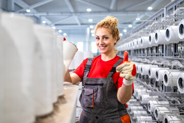 Female textile factory worker with thread spools holding thumbs up.