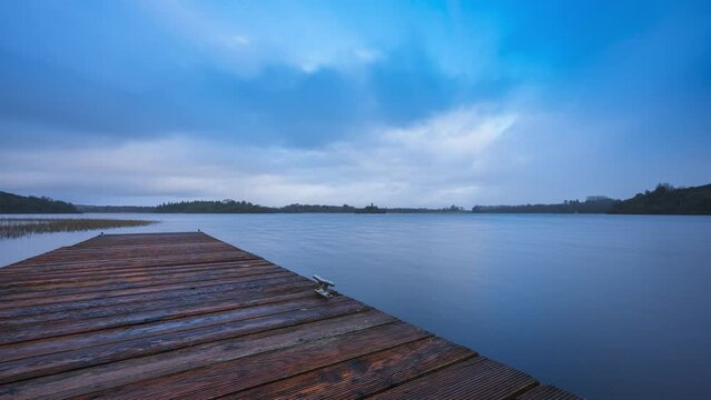 Time lapse of a timber lake pier in the foreground and castle ruin island with forest in distance on a cloudy sunny day at Lough Key in county Roscommon in Ireland.