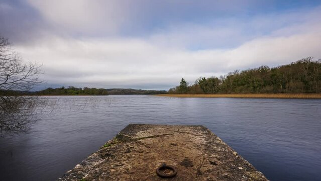 Time lapse of a concrete lake pier with forest in distance on a cloudy sunny day at Lough Key in county Roscommon in Ireland.