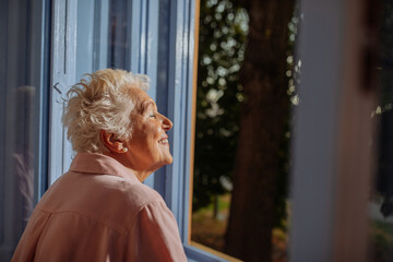 Elderly woman feeling the breeze trough the window