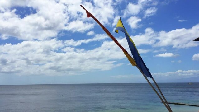 Two flags on poles on the beautiful beach in Siquijor Island in the Philippines. The clouds in the blue sky on the tropical island in the Philippines. A yellow and blue flag on the beach.