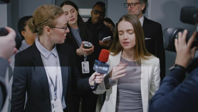 Confident female politician answers press questions and gives interview to the media walking in hallway of government building. Busy diplomat surrounded by crowd of news journalists. Press conference.