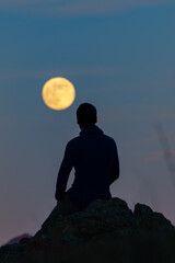 Hombre sentado mirando a la Luna - obrazy, fototapety, plakaty