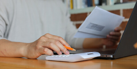 close up young man hand press on calculator and open over group of invoice letter mail from bank...