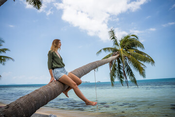 Kobieta siedzi na palmie nad wodą na rajskiej plaży