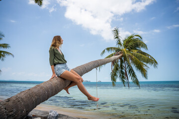 Kobieta siedzi na palmie nad wodą na rajskiej plaży
