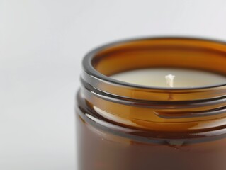 A candle is lit in a glass jar. The jar is brown and has a clear top
