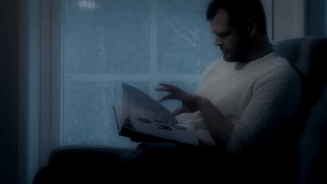 man reading book by window at night, snowing moonlight
