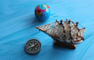 Sea Travel Concept Image. Globe, Wooden Ship Model And Vintage Compass On Blue Surface Symbolizing Ocean 
