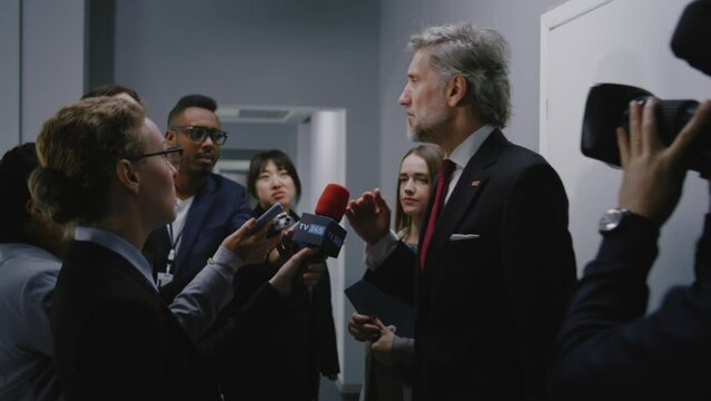 Busy minister of United States answers press questions, gives interview for media in hallway of government building. Republican politician surrounded by crowd of news journalists. Hot button issues.