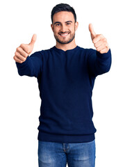 Young handsome man wearing casual clothes approving doing positive gesture with hand, thumbs up smiling and happy for success. winner gesture.