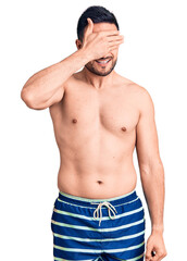 Fototapeta premium Young handsome man wearing swimwear smiling and laughing with hand on face covering eyes for surprise. blind concept.