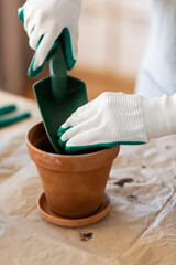 people, gardening and planting concept - close up of woman in gloves with trowel pouring soil to flower pot at home - 767714089