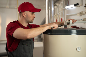 A professional technician wearing a red uniform is diligently working on maintaining a boiler in a...