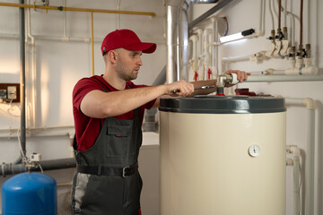 A man wearing a red shirt is shown fixing a water heater. He carefully inspects the heater,...