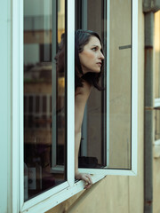 Elegant woman in the window looking outside. Reflection of buildings on the glass