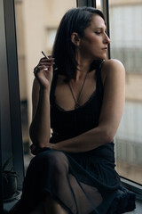 Beautiful and elegant woman sits by the window and smokes a cigarette