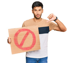 Young handsome man holding prohibited warning banner with angry face, negative sign showing dislike...