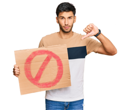 Young handsome man holding prohibited warning banner with angry face, negative sign showing dislike with thumbs down, rejection concept