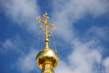 Golden dome of the Orthodox Church with a cross against the blue sky with white clouds. Christian...