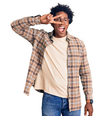 Handsome african american man with afro hair wearing casual clothes and glasses doing peace symbol with fingers over face, smiling cheerful showing victory