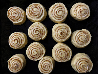 preparing homemade round cinnamon scrolls in a rectangular black baking pan, ready for baking