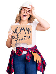 Young caucasian woman holding woman power banner smiling happy doing ok sign with hand on eye looking through fingers