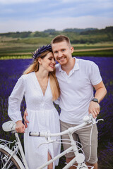 A young couple with a white bicycle standing in a field full of lavender in a state of happiness
