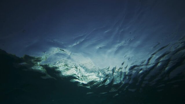 Sun glistens as crashing ocean wave mist foam spreads on surface, underwater looking up