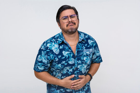 A pitiful middle aged man in a a hawaiian shirt looking very hungry, holding his grumbling stomach. Isolated on a white background.