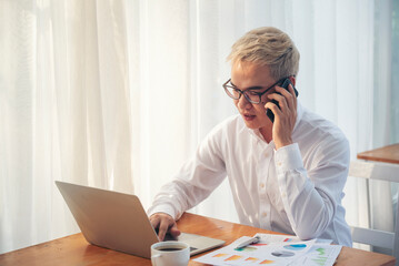 Asian Businessman using laptop calling phone at office desk. Man wear eye glasses talking...