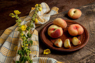 Clay plate with cut and whole saturn peaches or flat peaches on wooden background with yellow...