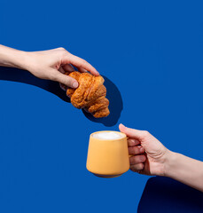 Women's hands hold fresh croissant and cup of coffee  on a blue background.