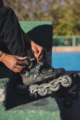Vertical photo of a latin man on the ground taking off or putting on his inline skates tying his...