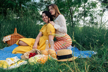 Two girls on a date sit on a blue blanket for a picnic in nature