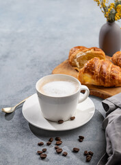 A cup of aromatic cappuccino coffee and fresh croissants on a blue background with coffee beans and flowers.