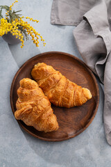 A fresh croissants in a wooden plate on a blue background with yellow flowers and napkin.