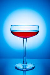 Flat champagne glass on a blue background. Red drink in a wineglass. Bright light shines through...