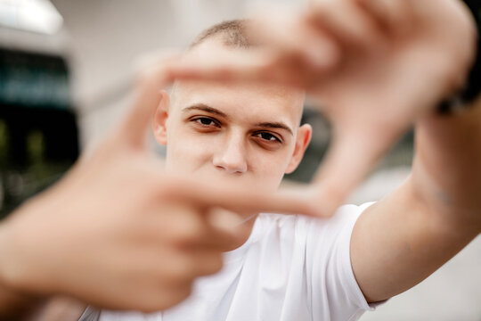 A man with a shaved head is holding his hands together in a frame. The image has a casual and relaxed mood, as the man is posing for a picture in a public space