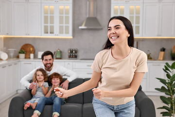 Happy family having fun at home. Mother dancing while her relatives resting on sofa