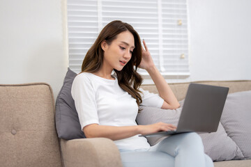 A young woman enjoys a leisurely day, comfortably using her laptop while reclining on a couch at home.